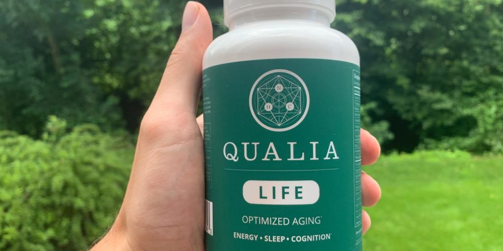 A hand holding one bottle of Qualia Life