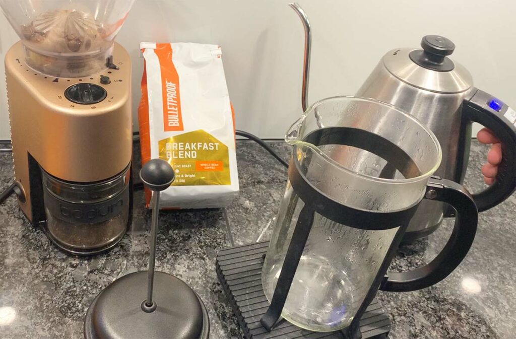 A bag of Bulletproof Breakfast Blend coffee next to a burr grinder, a gooseneck kettle and a French-press coffee maker