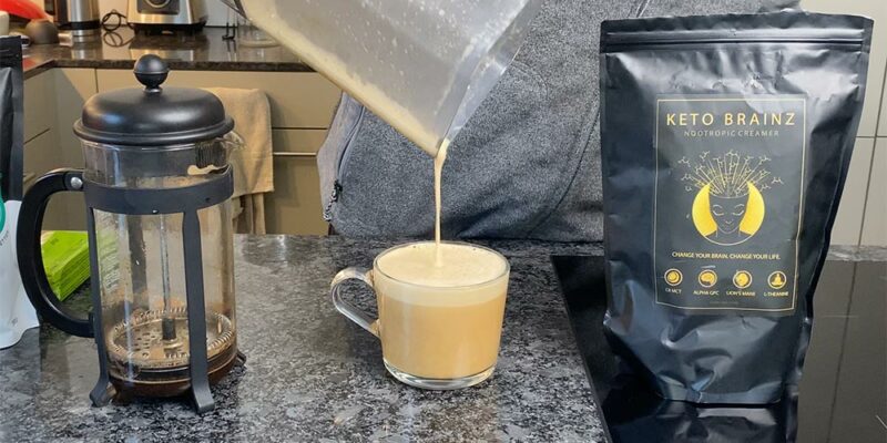 A cup of coffee and a French Press next to a bag of Keto Brainz
