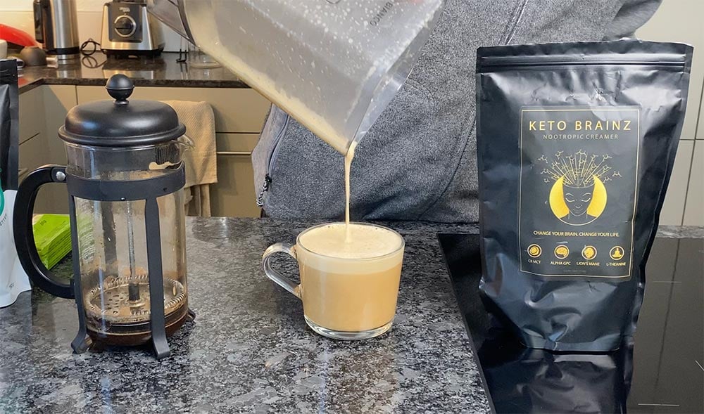 A cup of coffee and a French Press next to a bag of Keto Brainz