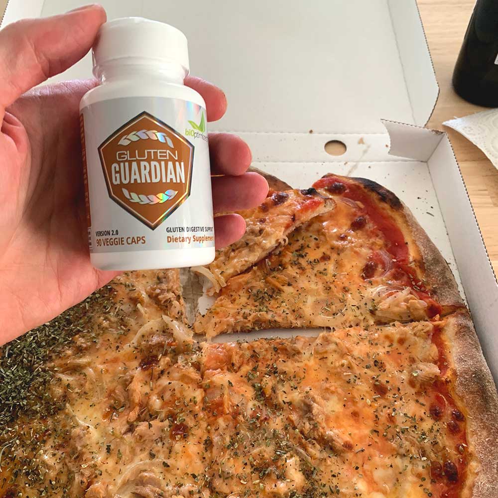 A hand holding a bottle of biOptimizers Gluten Guardian infront of a Pizza