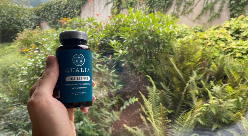 A bottle of Qualia Resilience infront of a lush green garden