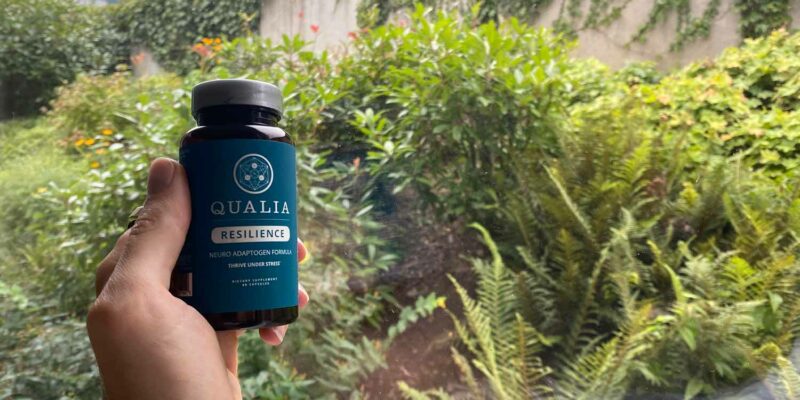 A bottle of Qualia Resilience infront of a lush green garden