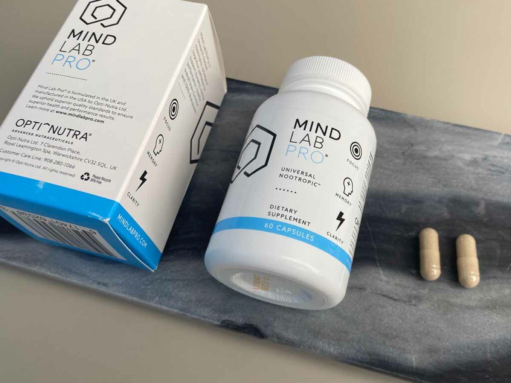 A box of Mind Lab Pro next to a bottle of Mind Lab next to 2 capsules on a marble tray