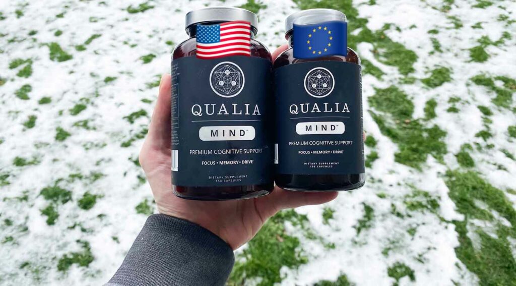 A hand holding one bottle of Qualia Mind US and one bottle of Qualia Mind EU