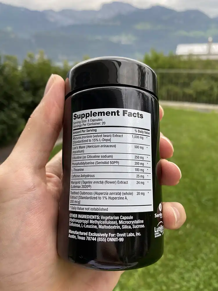 A hand holding a bottle of Onnit Alpha Brain Black Label showing Supplement Facts