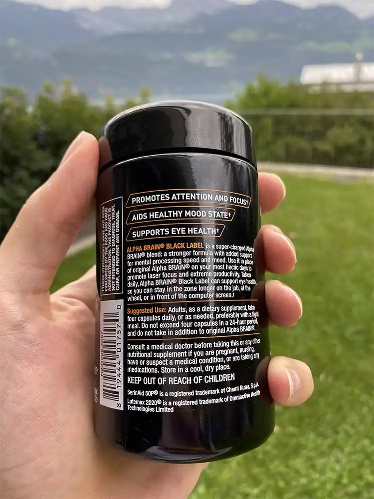 A hand holding a bottle of Onnit Alpha Brain Black Label showing dosage instructions