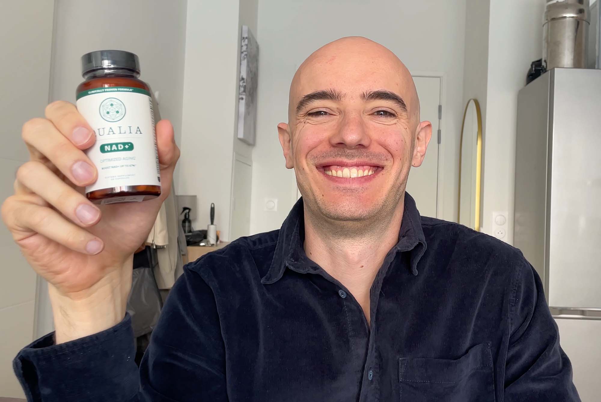 Max Hug smiling and holding a bottle of Qualia NAD+ supplement during his 3-month product review for boosting NAD+ levels and energy.